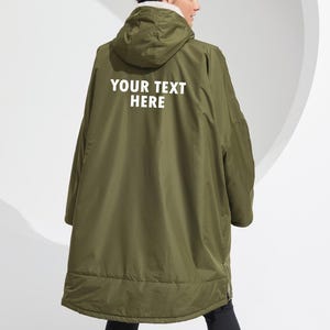 May include: An olive green hooded coat with the text "YOUR TEXT HERE" in white. The coat features a white fleece lining around the hood and a full-length zip. The coat is designed to be worn over other clothing.