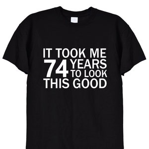 May include: Black t-shirt with white text that reads "It took me 74 years to look this good."
