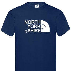 Peut inclure: Un t-shirt bleu marine avec un motif blanc représentant une chaîne de montagnes et le texte "NORTH YORKSHIRE" avec un symbole de marque déposée.