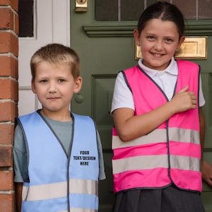 May include: Two children wearing high-visibility vests. One is light blue, the other is pink. Both have reflective silver stripes and a black trim. The light blue vest has the text "YOUR TEXT/DESIGN HERE".