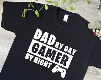 May include: Black t-shirt with white text that reads "Dad by Day Gamer by Night" and a white video game controller graphic.