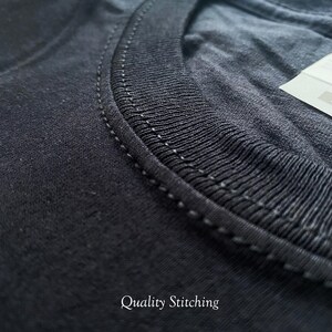 May include: A black t-shirt featuring a ribbed crew neckline with reinforced double-needle stitching along the collar seam. A white fabric care label is partially visible at the top right corner. The text Quality Stitching is printed below.