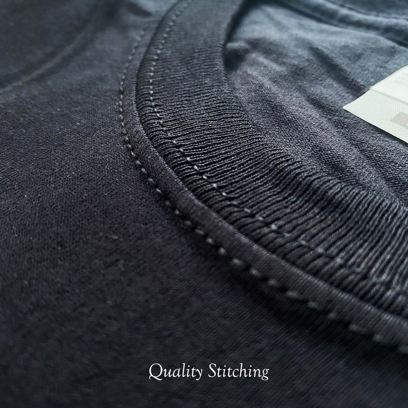 May include: A black t-shirt featuring a ribbed crew neckline with reinforced double-needle stitching along the collar seam. A white fabric care label is partially visible at the top right corner. The text Quality Stitching is printed below.