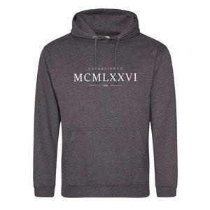 May include: A dark gray hooded sweatshirt with the text "ESTABLISHED MCMILXXVI 1976" printed on the front.