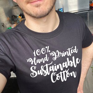 May include: A black t-shirt with white text that reads "100% Hand Printed Sustainable Cotton".