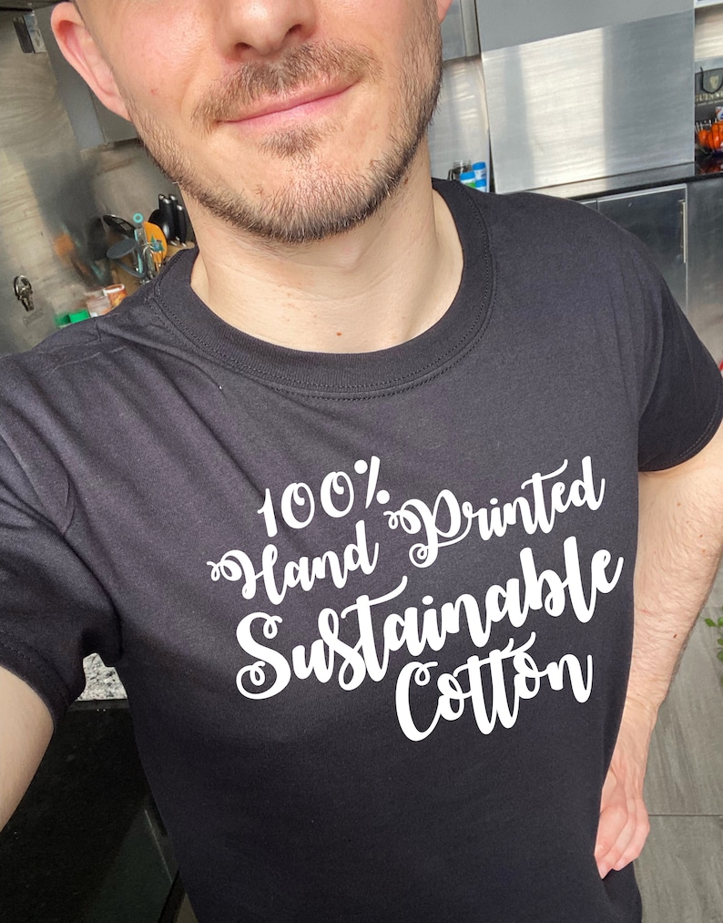May include: A black t-shirt with white text that reads "100% Hand Printed Sustainable Cotton".