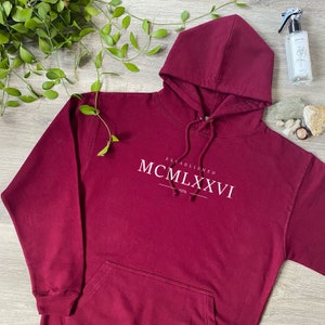 May include: Burgundy hooded sweatshirt with the text "Established MCM LXXVI 1976" printed on the front.