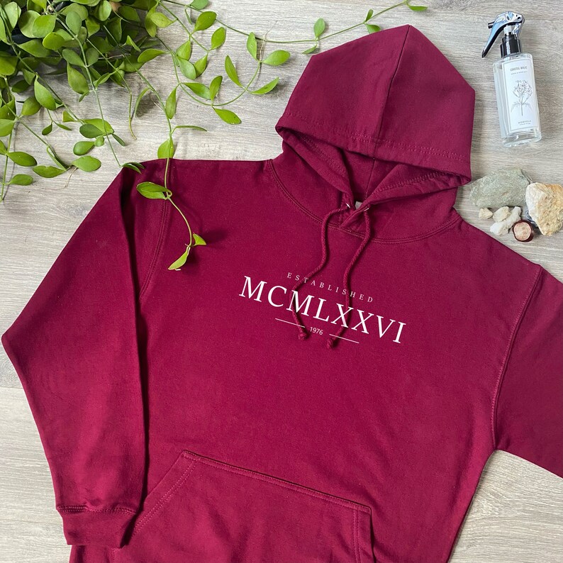 May include: Burgundy hooded sweatshirt with the text "Established MCM LXXVI 1976" printed on the front.