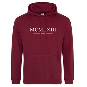 Puede incluir: Sudadera con capucha color burdeos con texto blanco que dice "MCMLXIII EST 1963".