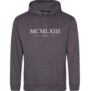 Puede incluir: Una sudadera con capucha gris oscuro con una impresi&oacute;n blanca que dice "MCMLXIII EST 1963".
