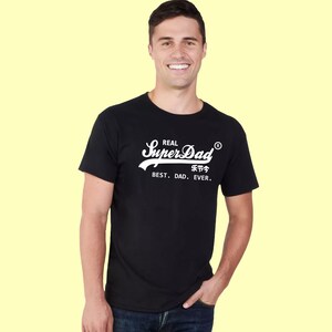 May include: A black short-sleeved t-shirt featuring white screen-printed text that reads Real SuperDad with a registered trademark symbol, followed by Chinese characters and the phrase BEST. DAD. EVER. in a clean, sans-serif font.