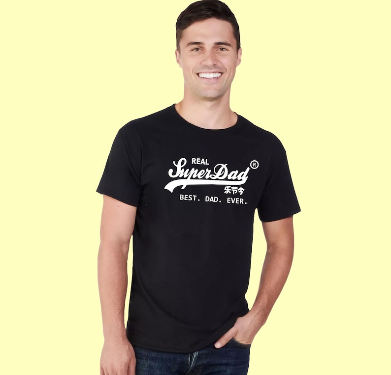 May include: A black short-sleeved t-shirt featuring white screen-printed text that reads Real SuperDad with a registered trademark symbol, followed by Chinese characters and the phrase BEST. DAD. EVER. in a clean, sans-serif font.