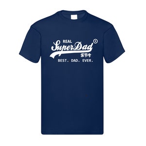 May include: A navy blue short-sleeved t-shirt featuring white screen-printed text that reads REAL SuperDad with a registered trademark symbol, Chinese characters, and the phrase BEST. DAD. EVER. centered on the chest area of the garment.