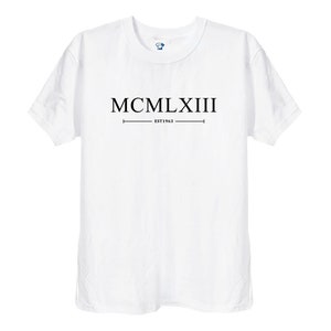 Puede incluir: Camiseta blanca con texto negro que dice "MCMLXIII EST 1963".