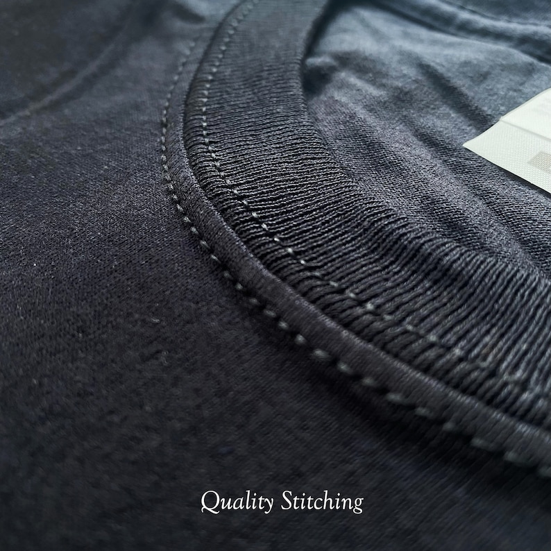 May include: Close-up of the neckline of a black t-shirt, showing the quality stitching. The stitching is a fine, even line, indicating a well-made garment.