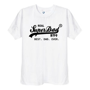 May include: A white short-sleeved t-shirt featuring black text on the chest that reads REAL SuperDad with a registered trademark symbol, followed by Chinese characters and the phrase BEST. DAD. EVER. in a clean, sans-serif font.