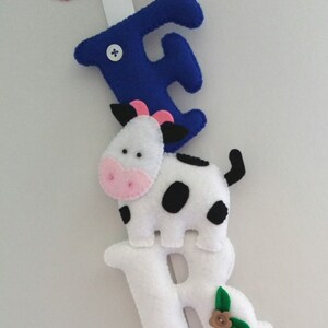 May include: A felt letter banner with the letters F, R, A, and a cow in between the F and R. The letters are white with black stitching and the cow is white with black spots. The F is blue and the A is green.
