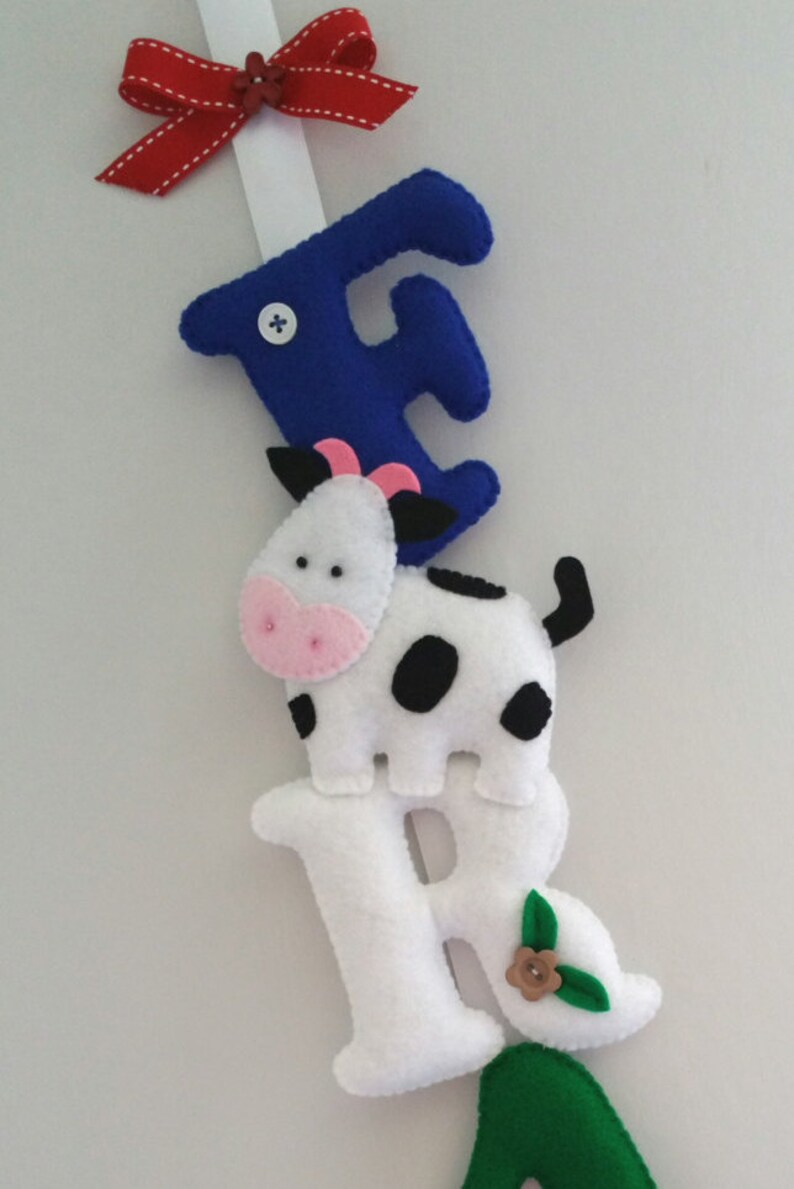 May include: A felt letter banner with the letters F, R, A, and a cow in between the F and R. The letters are white with black stitching and the cow is white with black spots. The F is blue and the A is green.