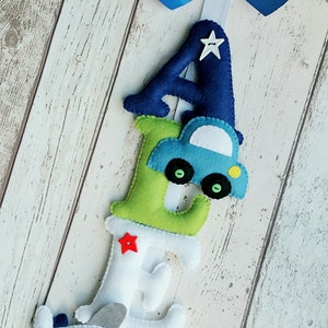 May include: A felt letter banner with the letters A, E, S, and a blue car and a gray airplane. The letters are in different colors, including blue, green, white, and red. Each letter has a red star button.