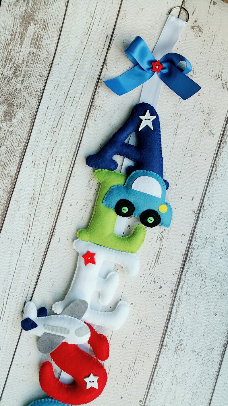 May include: A felt letter banner with the letters A, E, S, and a blue car and a gray airplane. The letters are in different colors, including blue, green, white, and red. Each letter has a red star button.