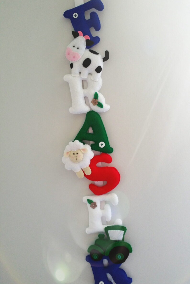 May include: A felt banner with the word "FARMER" spelled out in colorful letters. Each letter has a different farm animal or farm-themed image attached to it. The letters are blue, white, green, red, white, and blue.