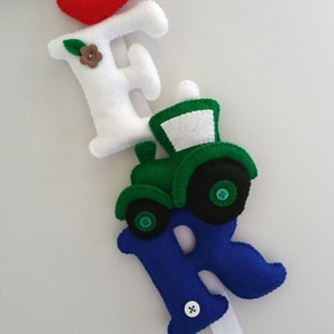 May include: A felt letter banner with the letters "E" and "R" in white and blue, respectively. A green felt tractor with black wheels is attached to the "E".