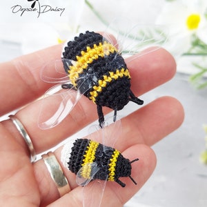 May include: Two crocheted bumblebees with black and yellow stripes and white accents. The bumblebees have clear plastic wings.
