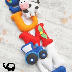 May include: A felt letter banner spelling out the word "SUMMER" with a cow, tractor, and flowers. The letters are in various colors, including blue, orange, red, white, and green.