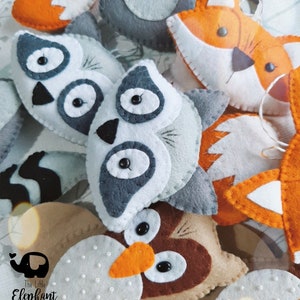 May include: A collection of felt animal ornaments, including a raccoon, fox, owl, and other woodland creatures. The ornaments are handmade and feature embroidered details and button eyes.