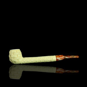 May include: Ivory-colored tobacco pipe with intricate carved basket weave and dotted patterns. The stem has a marbled orange and brown finish. The pipe is set against a black background, with its reflection visible below.