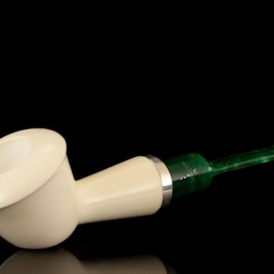 May include: A white meerschaum pipe with a green acrylic stem. The pipe is made of a smooth, white material and has a classic shape.