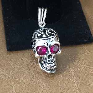 May include: A silver skull pendant with intricate detailing and two pink gemstone eyes.