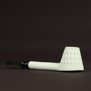Puede incluir: Una pipa de tabaco blanca con un tallo texturizado y una cazoleta cónica. La cazoleta presenta un patrón de cortes en forma de lágrima. La boquilla es negra y la pipa está sobre un fondo marrón oscuro.