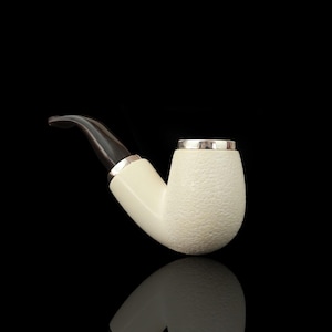 May include: Ivory-coloured smoking pipe with a textured bowl and a dark, curved stem. The pipe features silver-coloured accents at the bowl's rim and the stem's base. The pipe is set against a black background.