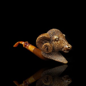 May include: A wooden pipe with a carved ram's head, the ram has brown fur and large curled horns. The pipe is made of a light brown wood with a darker brown stem.