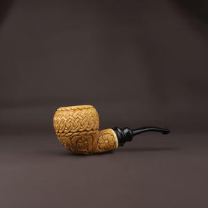 May include: A carved tobacco pipe with a light brown bowl featuring a woven pattern and floral designs. The stem is black with a curved mouthpiece. The pipe is a classic smoking accessory.