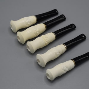 May include: Six white cigarette holders with black and gold accents. The holders have a carved design and are arranged in a row.