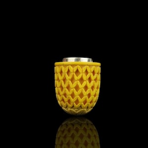 May include: A yellow, carved container with a silver top. The container has a repeating diamond pattern. The bottom of the container has a decorative, leaf-like design. The container is set against a black background.
