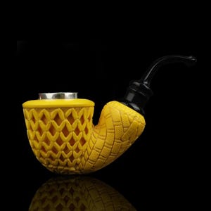 May include: A yellow tobacco pipe with a carved diamond pattern on the bowl and a textured design on the stem. The mouthpiece is black, and the rim of the bowl is silver. The pipe is set against a black background.