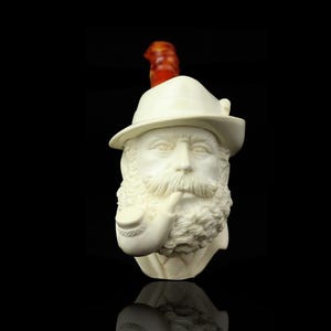 May include: Ivory-colored bust of a man with a long beard, mustache, and hat, smoking a pipe. The pipe has a curved stem. A red-orange accent sits atop the hat. The bust is set against a black background.