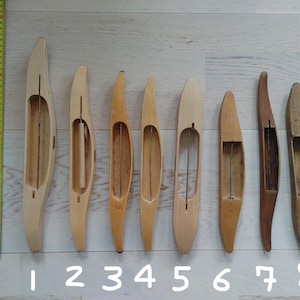 Puede incluir: Ocho lanzaderas de tejido de madera de varios tamaños y colores, dispuestas en fila. Las lanzaderas varían de tonos de madera claros a oscuros, con una cinta métrica en el lado izquierdo. Los números del 1 al 8 están escritos debajo.