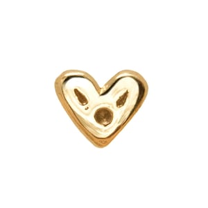May include: A small, gold-colored heart-shaped charm. The charm has a rounded shape with a small hole in the center and two smaller holes near the top. The charm is set against a white background.