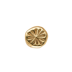 May include: A gold-toned metal charm with a raised, circular design resembling a stylized flower.