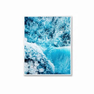 May include: An aerial photograph of a blue ocean with white foamy waves crashing against each other. The water is a vibrant blue and the waves are white and foamy.