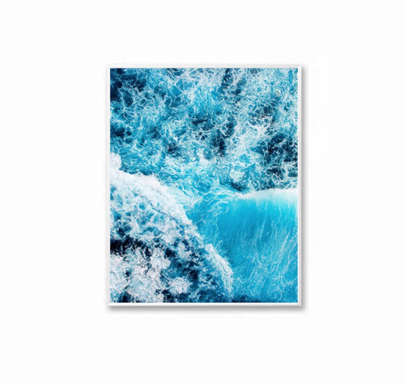 May include: An aerial photograph of a blue ocean with white foamy waves crashing against each other. The water is a vibrant blue and the waves are white and foamy.