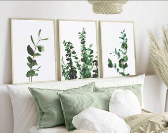 May include: Three framed prints of green eucalyptus leaves on a white background. The prints are hanging on a white wall above a bed with green and white pillows.