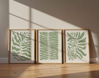 Op de afbeelding: Een set van drie rechthoekige wandkunstprints in lichte houten lijsten. Elke print toont een botanische illustratie van varenachtige bladeren in saliegroen op een crèmekleurige achtergrond, opgesteld in een rij.