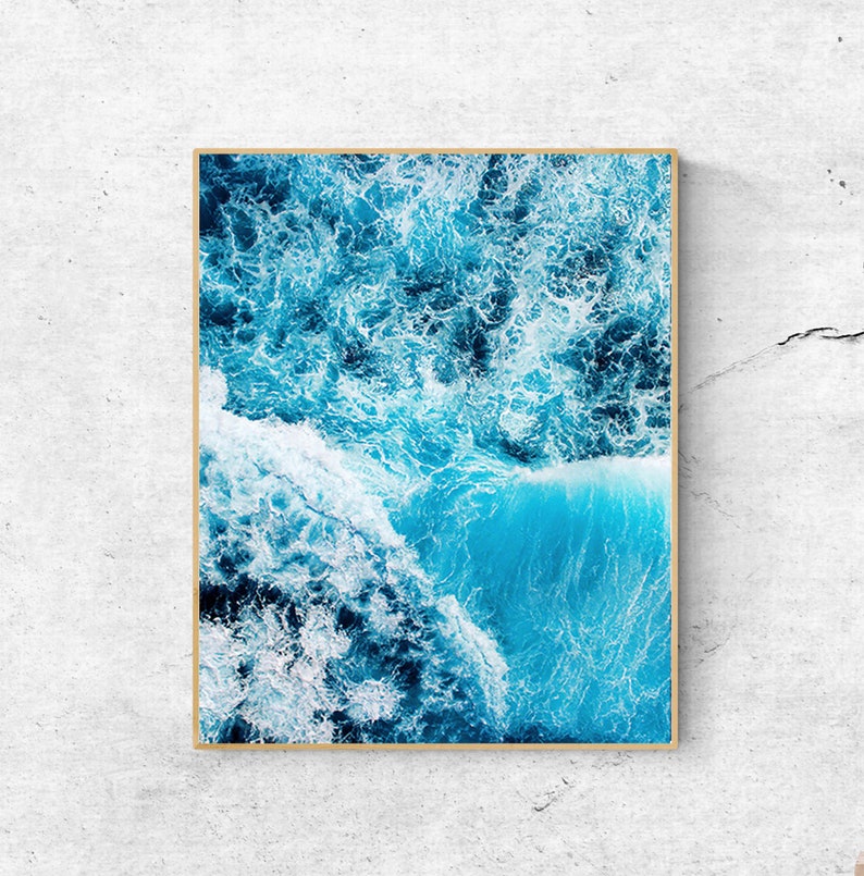May include: An aerial view of a blue ocean with white foamy waves crashing. The water is a vibrant blue and the waves are white and foamy. The image is taken from a high angle, giving a unique perspective of the ocean.