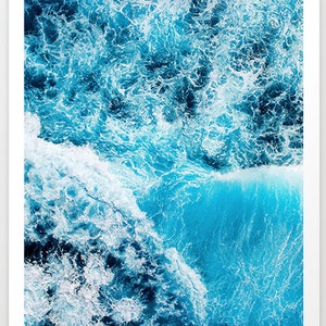 May include: An aerial view of a turquoise blue ocean with white foamy waves crashing.