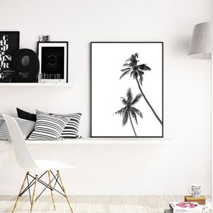 May include: Black and white framed print featuring two palm trees against a white background. The artwork is displayed on a white shelf with decorative items, including pillows, a chair, and other framed art.